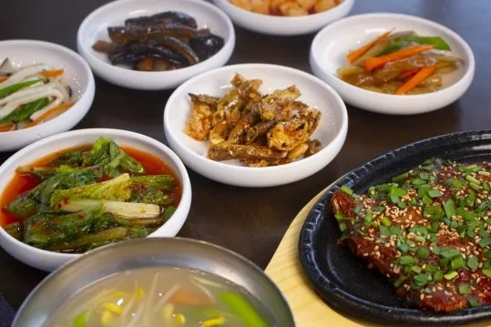 밑반찬 여러 접시와 오른쪽 돌판 황태구이, 앞쪽 맑은 국 그릇