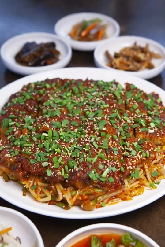 흰 큰 접시에 콩나물을 깔고 올린 양념 황태 요리(부추·깨), 뒤로 반찬 세 접시